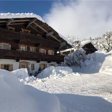 A cozy wooden house in a snowy landscape. The snow is high and the sky is clear and blue.