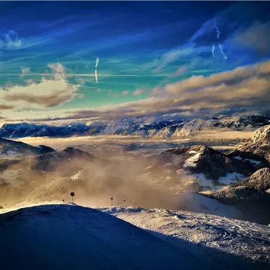 Eine beeindruckende Berglandschaft mit schneebedeckten Gipfeln und Wolken. Der Himmel ist klar und zeigt wunderschöne Farbtöne.
