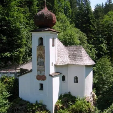 A small, white chapel stands surrounded by lush greenery. The characteristic onion dome harmoniously rises into the landscape.