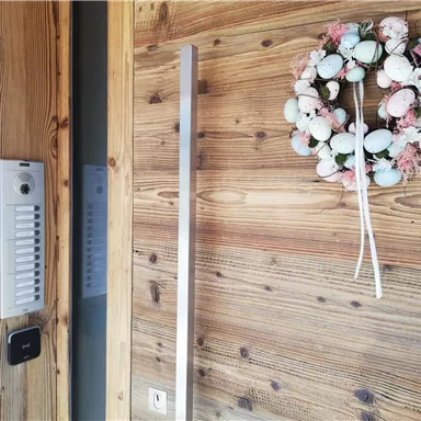 A wooden wall with a modern intercom system and a festive wreath made of eggs and flowers. The entrance appears welcoming and friendly.