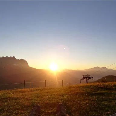 Ein schöner Sonnenuntergang über den Bergen. Die Landschaft ist friedlich mit Grasflächen und Felsen im Hintergrund.