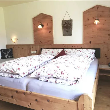 A cozy bedroom with a wooden bed and beautiful bedding. The walls are made of wood, and there is soft light from the wall lamps.