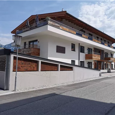 A modern building with several floors and wooden balconies. It is located on a street and has a clear sky in the background.