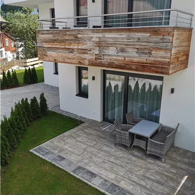 A modern apartment with wooden cladding on the balcony. The outdoor area is designed with lawn and a small hedge.