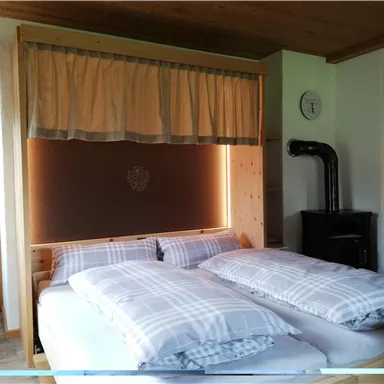 A cozy bedroom with a large bed and plaid blankets. The walls are made of wood and there is a small stove.