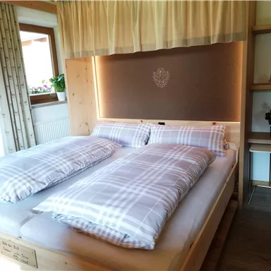 A cozy bedroom with a large double bed and plaid blankets. The room is well-lit and has a warm, inviting atmosphere.