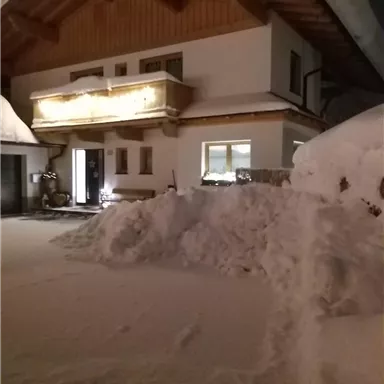 Ein gemütliches Haus im Schnee, umgeben von einer dicken Schneeschicht. Beleuchtung sorgt für eine einladende Atmosphäre in der Nacht.