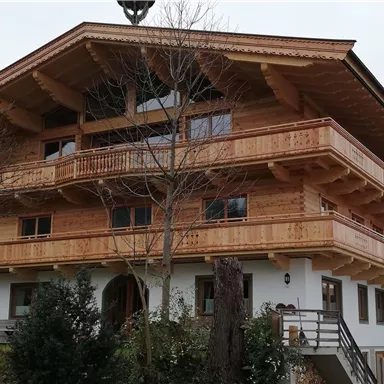 A traditional wooden house with several balconies and large windows. Surrounding the house are trees and small bushes.