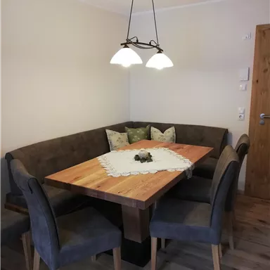 A cozy dining area with a wooden table and a corner bench. The chairs are gray and an attractive lamp hangs over the table.