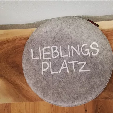 A round gray seat with the print "FAVOURITE SPOT". It is located on a wooden surface.