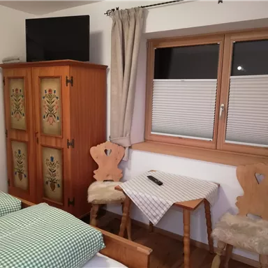 A cozy room with two beds and a wooden wardrobe. By the window, there is a table and two chairs.