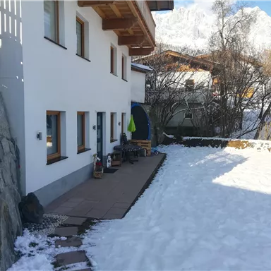 A cozy house in a winter landscape with snow. In the background, snow-covered mountains are visible.