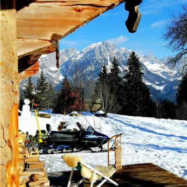 A picturesque winter landscape with snow-covered mountains in the background. In the foreground, there is a cozy cabin and some equipment for winter sports.