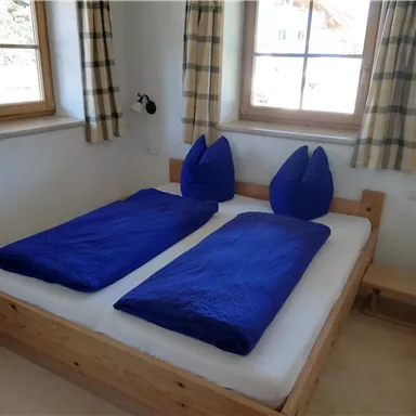 Ein gemütliches Schlafzimmer mit zwei getrennten Betten und blauen Bettdecken. Die Fenster lassen viel Tageslicht herein und die Wände sind hell gestrichen.