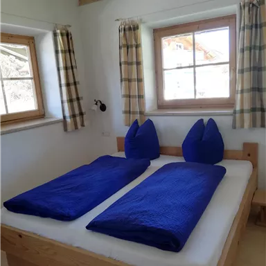 Ein gemütliches Schlafzimmer mit zwei Einzelbetten und blauen Bettdecken. Große Fenster sorgen für viel Tageslicht.