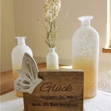 A decorative arrangement with two vases and a wooden sign. The sign reads: "Happiness begins where you forget about time."