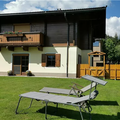 A cozy house with wooden elements and a well-maintained garden. Two loungers are outside to enjoy the sun.