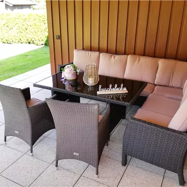 A cozy outdoor area with a side table group and a cushioned seating corner. The space is bright and inviting, surrounded by greenery.