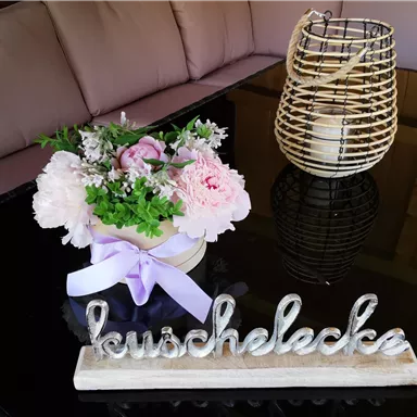 An elegant decoration on a table with a flower arrangement in soft colors and a sign that reads "cuddle corner." In the background, there is a stylish lantern.
