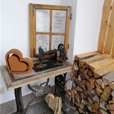 Ein alter Nähmaschine auf einem Tisch neben einem Stapel Holz. Im Hintergrund befindet sich ein Fenster mit handgeschriebenen Notizen.