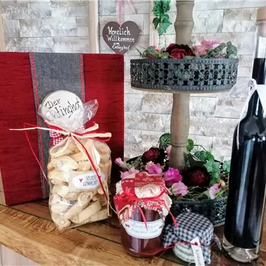 Eine dekorative Präsentation mit einem roten Buch, Keksen, Marmelade und einer Flasche. Darüber hinaus sind Blumen und eine Willkommensnachricht zu sehen.