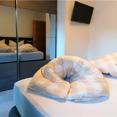 A cozy bedroom with a bed and pillows. In the background, a mirror and a television are visible.