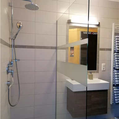 A modern bathroom with a glass shower and a simple vanity. The walls are tiled in light colors and the lighting creates a pleasant atmosphere.