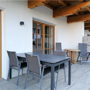 A modern terrace with a table and chairs. The walls are bright and the roof provides protection from sun and rain.