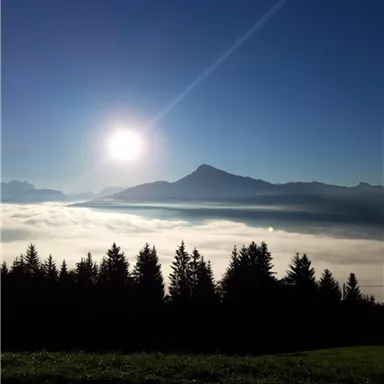 Eine beeindruckende Berglandschaft mit tief hängenden Wolken und strahlendem Sonnenlicht. Der Himmel ist klar und blau.