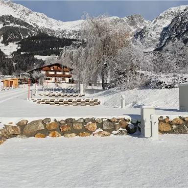 A winter landscape with snow-covered mountains and a quiet farmhouse. The ground is covered with fresh snow, and the surroundings appear peaceful and idyllic.