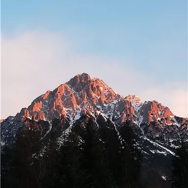 Ein majestätischer Berg mit schneebedecktem Gipfel. Der Himmel ist klar und die Sonne beleuchtet die Felsen in warmen Farben.