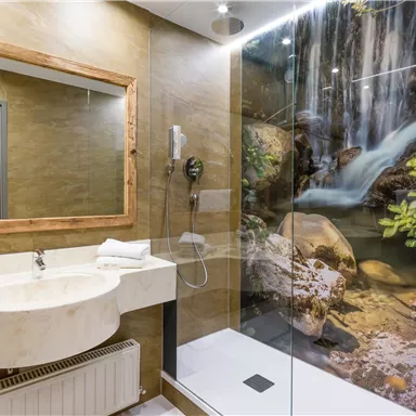 Ein modernes Badezimmer mit einem Waschbecken aus Marmor und einer großen Dusche. Im Hintergrund sieht man ein Wandbild mit einem Wasserfall und grünen Pflanzen.