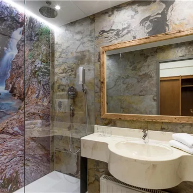 Ein modernes Badezimmer mit einer Glasdusche und einem großen Spiegel. Die Wände sind mit einem schönen Naturmotiv dekoriert, das einen Wasserfall zeigt.