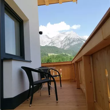 A balcony with two chairs and a view of the mountains. The sky is blue and the landscape is green.
