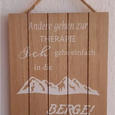 Ein Holzschild mit der Aufschrift: "Andere gehen zur THERAPIE, ich gehe einfach in die BERGE!" Es zeigt stilisierte Berge und hat eine rustikale, natürliche Ausstrahlung.
