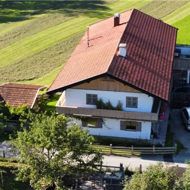 A traditional house with a red roof in a rural setting. View of a well-kept garden and parked cars.