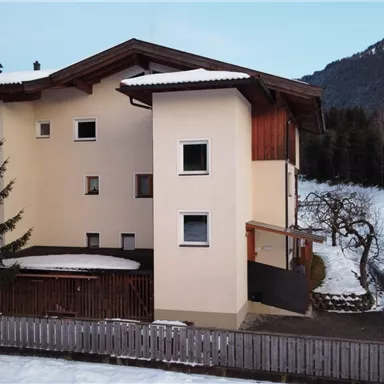 A modern building in the snow with a tree in the foreground. In the background, snow-covered mountains can be seen.
