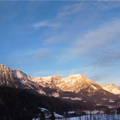 An impressive mountain landscape under a clear sky. The snow-covered peaks are bathed in warm light.