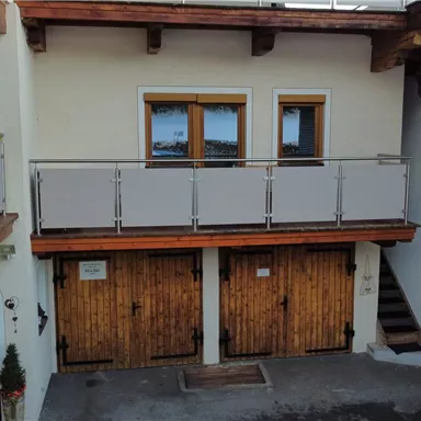 A building with a balcony and two wooden doors on the ground floor. In the background, windows are visible, and the facade is bright and inviting.