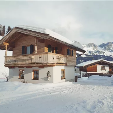 A charming chalet in the snow with mountains in the background. The surroundings are wintry and tranquil.