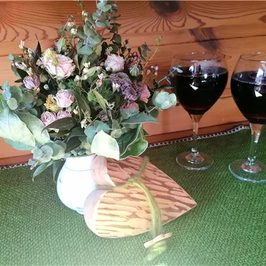 Ein hübsches Blumenarrangement in einer weißen Vase steht neben zwei Gläsern mit dunklem Getränk. Im Hintergrund ist eine grüne Tischdecke zu sehen.