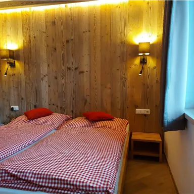 A cozy room with two single beds and checked bedding. The walls are made of wood and there is soft lighting.