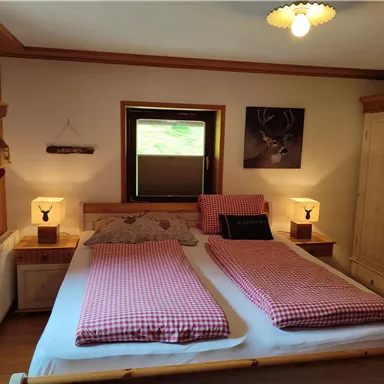 A cozy bedroom with a double bed and checked bedspreads. The wood paneling and soft lighting create an inviting atmosphere.