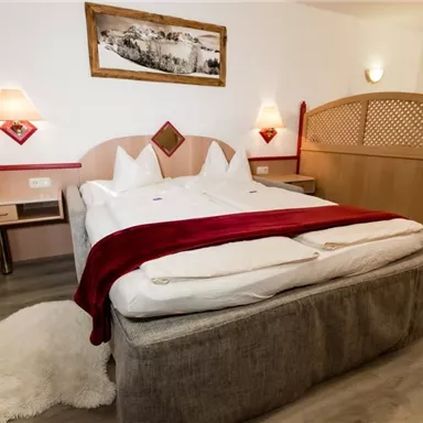 Ein gemütliches Schlafzimmer mit einem großen Bett und eleganter Bettwäsche. Die Wände sind hell, und es gibt Holzmöbel sowie ein Bild an der Wand.