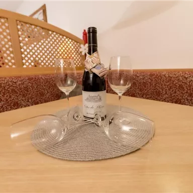 Eine Flasche Wein steht auf einem Tisch, umgeben von zwei Weingläsern. Der Tisch ist mit einem runden Platzdeckchen dekoriert.