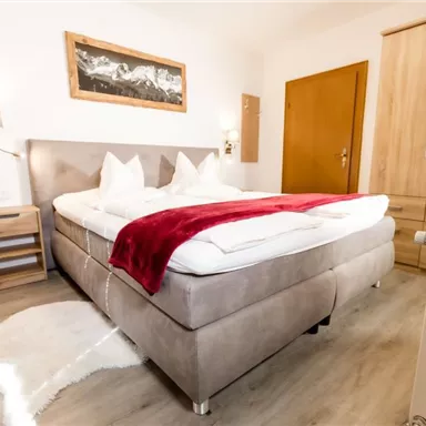 Ein gemütliches Schlafzimmer mit einem großen Doppelbett und weißen Kopfkissen. Holzschränke und sanfte Farben schaffen eine einladende Atmosphäre.