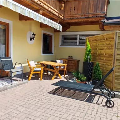 Ein gemütlicher Außenbereich mit einer Sitzecke und einem Sonnenschirm. Die Terrasse ist von einem Holzzaun und Pflanzen umgeben.