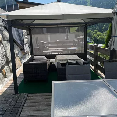 Ein gemütlicher Außenbereich mit einem Pavillon und Sitzmöbeln. Der Blick auf die umliegenden Berge und die grüne Landschaft ist beeindruckend.