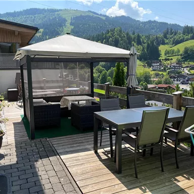 Ein gemütlicher Außenbereich mit einem Pavillon und einem Esstisch. Umgeben von einer schönen Landschaft und grünen Hügeln.