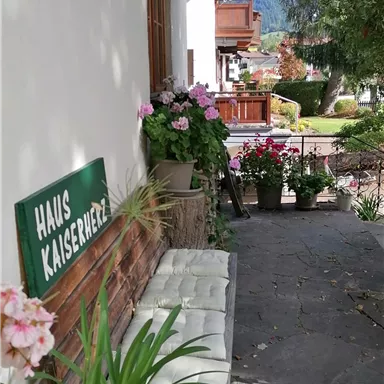 Ein schöner Eingangsbereich mit Blumen und einer Bank. Das Schild "Haus Kaiserblick" fügt einen charmanten Akzent hinzu.